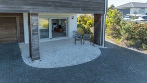 Una casa moderna con garaje, un patio cubierto con dos sillas y un camino de entrada de grava.