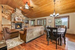 Ein gemütliches Wohnzimmer mit Kamin aus Stein, Holzboden und einem Essbereich mit Holztisch und Stühlen.