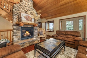 A cozy living room with a stone fireplace, wooden ceiling, and a brown leather sofa.