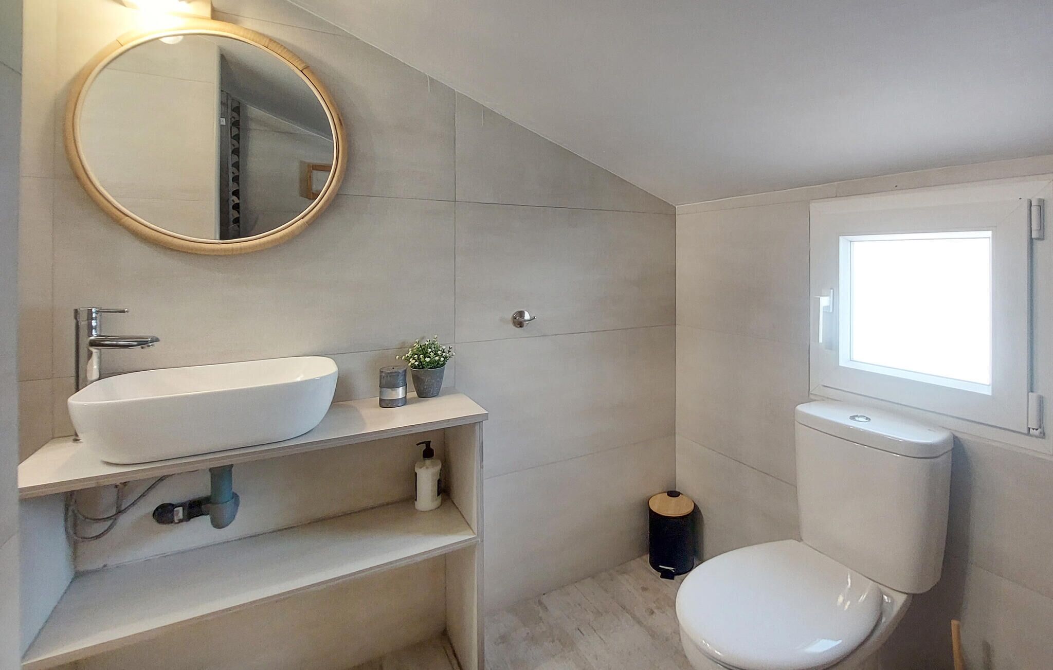 Un baño moderno con un espejo redondo, un lavabo blanco, un inodoro y una pequeña ventana.