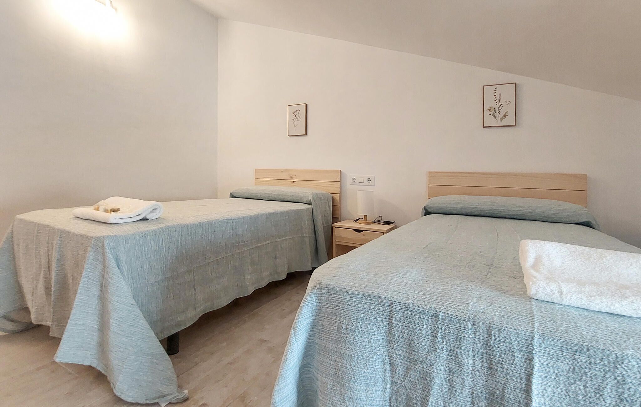 Ein Hotelzimmer mit zwei Einzelbetten, einem kleinen Nachttisch mit Lampe und einer Wandsteckdose.