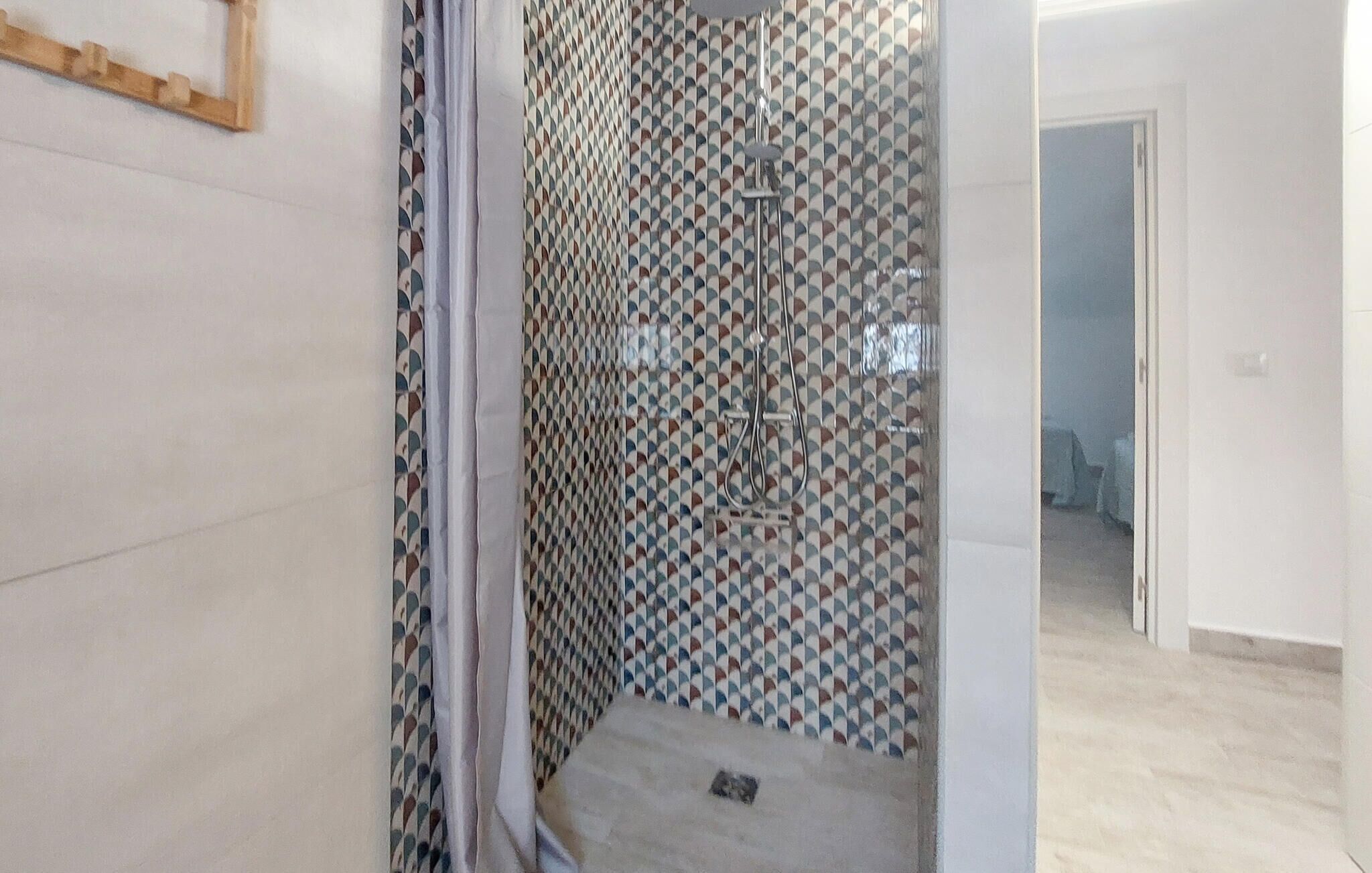 A bathroom with patterned tiles, a shower, and a visible door leading to another room.