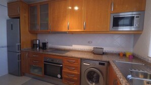 Une cuisine dotée de meubles en bois, d’un réfrigérateur en acier inoxydable, d’un four à micro-ondes, d’une machine à café, d’un lave-linge et d’un évier.