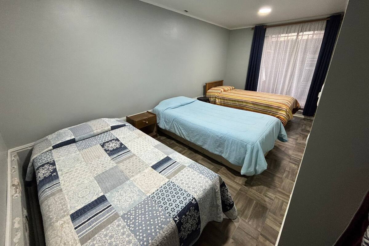 A bedroom with two beds, a wooden floor, and a window with curtains.
