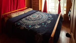 A wooden cabin bedroom with a bed, a dresser, and a window with red curtains. - CASA EL CANELO (El Quisco)