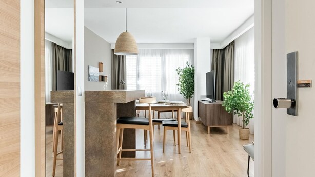 Moderni, avoimen pohjaratkaisun mukainen olohuone ja ruokailutila, jossa on puulattia, ruokapöytä tuoleineen, riippuvalaisin, televisio ja ruukkukasvi.
