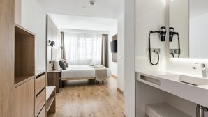Moderni hotellihuone, jossa on sänky, yöpöytä, vaatekaappi ja suuri peili, jonka yhteydessä on puhelin.