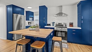 Een moderne keuken met blauwe kastjes, een houten eiland, roestvrijstalen apparatuur en een witte tegelachtergrond.