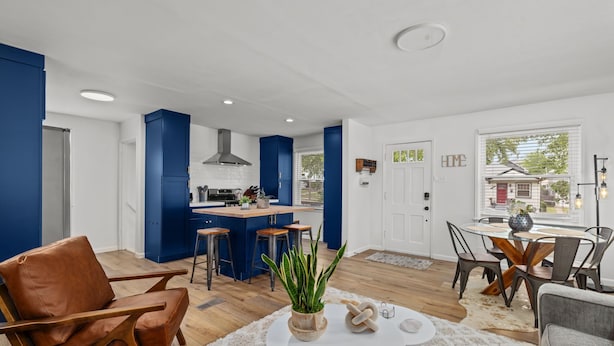 Een moderne keuken met blauwe kastjes, een centraal eiland met krukken, en een eethoek met een ronde tafel en stoelen.