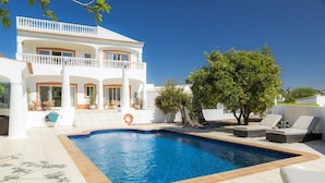 Une maison à deux étages avec une piscine, un espace salon extérieur et un arbre.