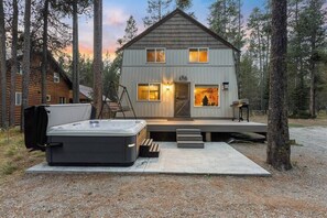 Une cabane en rondins à deux étages, dotée d’un bain à remous et d’un espace extérieur aménagé, située dans un cadre forestier.