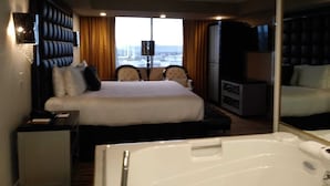 A hotel room with a large bed, a sitting area with chairs, a desk, a minibar, a television, and a bathtub. - Las Vegas Formula 1 Weekend Nov21 2025 (Las Vegas)
