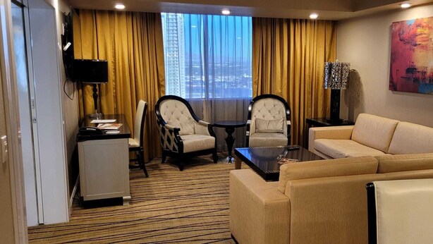 A hotel room with a sofa, two armchairs, a coffee table, a TV, and a large window with a city view. - Las Vegas Formula 1 Weekend Nov21 2025 (Las Vegas)