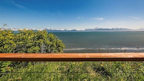 A view of a lake with mountains in the background, a wooden fence in the foreground, and greenery around. - Oceanfront Luxury Suite Overlooking Kachemak Bay and Homer Spit! (Homer)