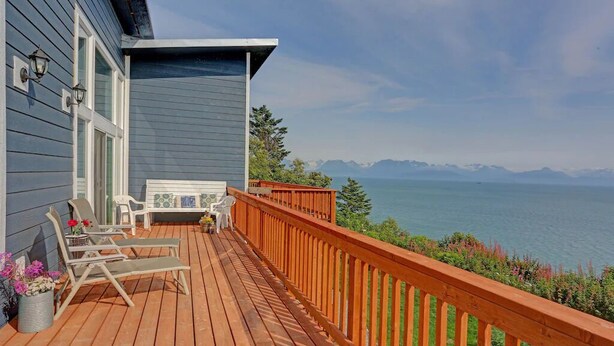 Une terrasse en bois avec deux chaises longues et une petite table, d’où l’on peut admirer un plan d’eau avec des montagnes à l’horizon.