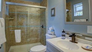 Un baño con ducha envuelta en vidrio, inodoro, lavamanos y tocador con armarios.