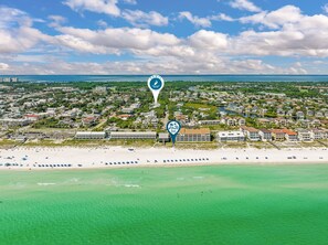 Vue aérienne d’une ville côtière avec une plage, des quartiers résidentiels et un port de plaisance.