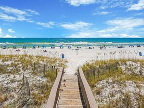 A wooden boardwalk leading to a beach with clear skies and calm waters.