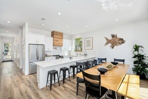 Une cuisine moderne avec des meubles blancs, un réfrigérateur en acier inoxydable et un îlot central en bois doté de tabourets de bar.