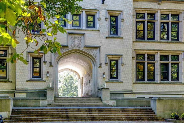 A building with a central archway leading to a staircase, surrounded by multiple windows and a brick facade.