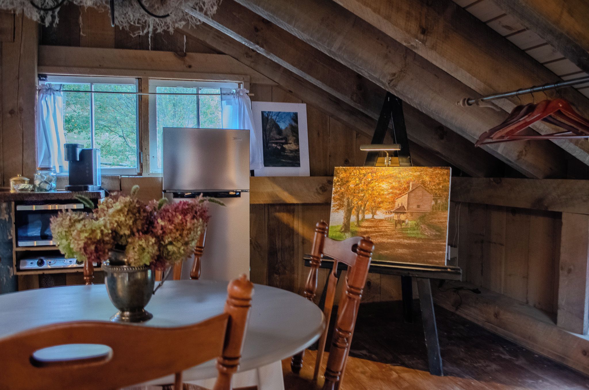 A rustic wooden interior with a dining table, chairs, a painting, and a television.