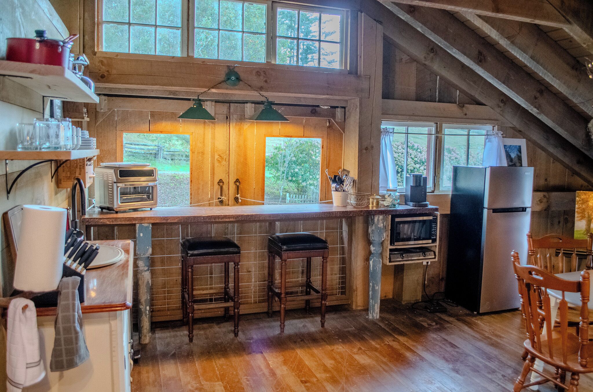 A rustic kitchen with wooden beams, a large window, and a bar area with stools.
