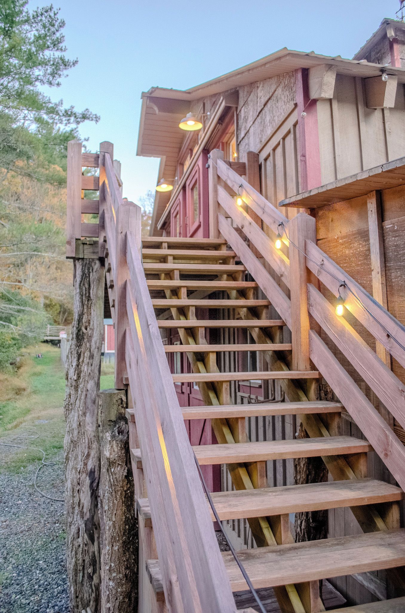 A wooden staircase leading to a building with a rustic design, featuring a wooden railing and string lights.