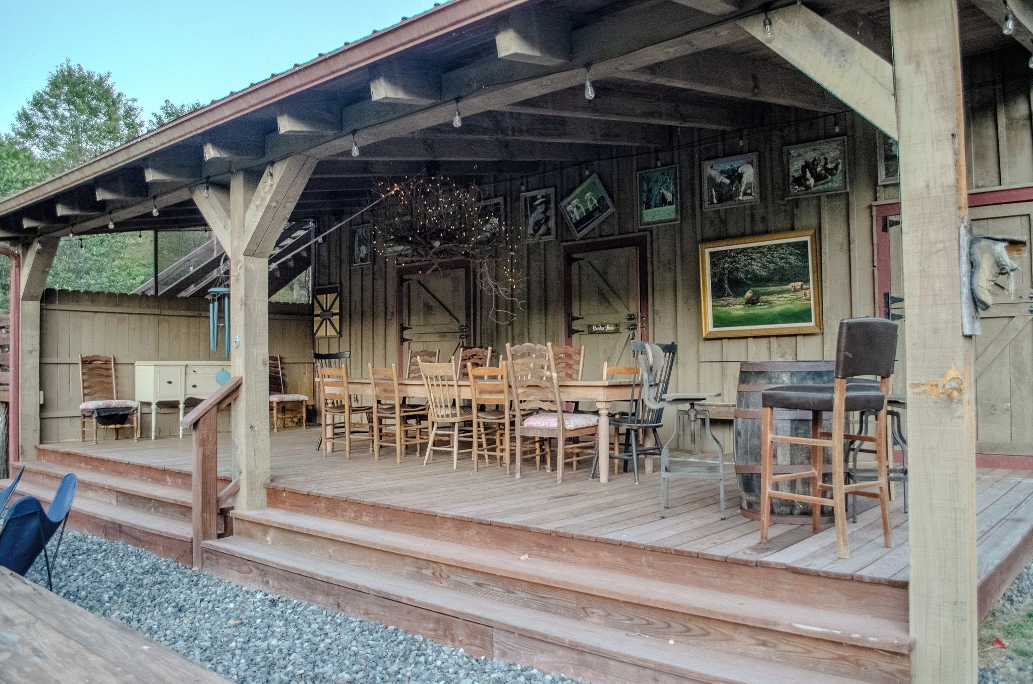 A wooden deck with a covered seating area, wooden chairs, a table, and a bar stool.