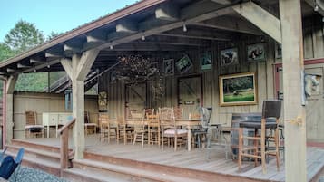 A wooden deck with a covered seating area, wooden chairs, a table, and a bar stool.