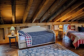Um quarto de sótão acolhedor com uma cama, uma pequena mesa com abajur e teto de madeira.