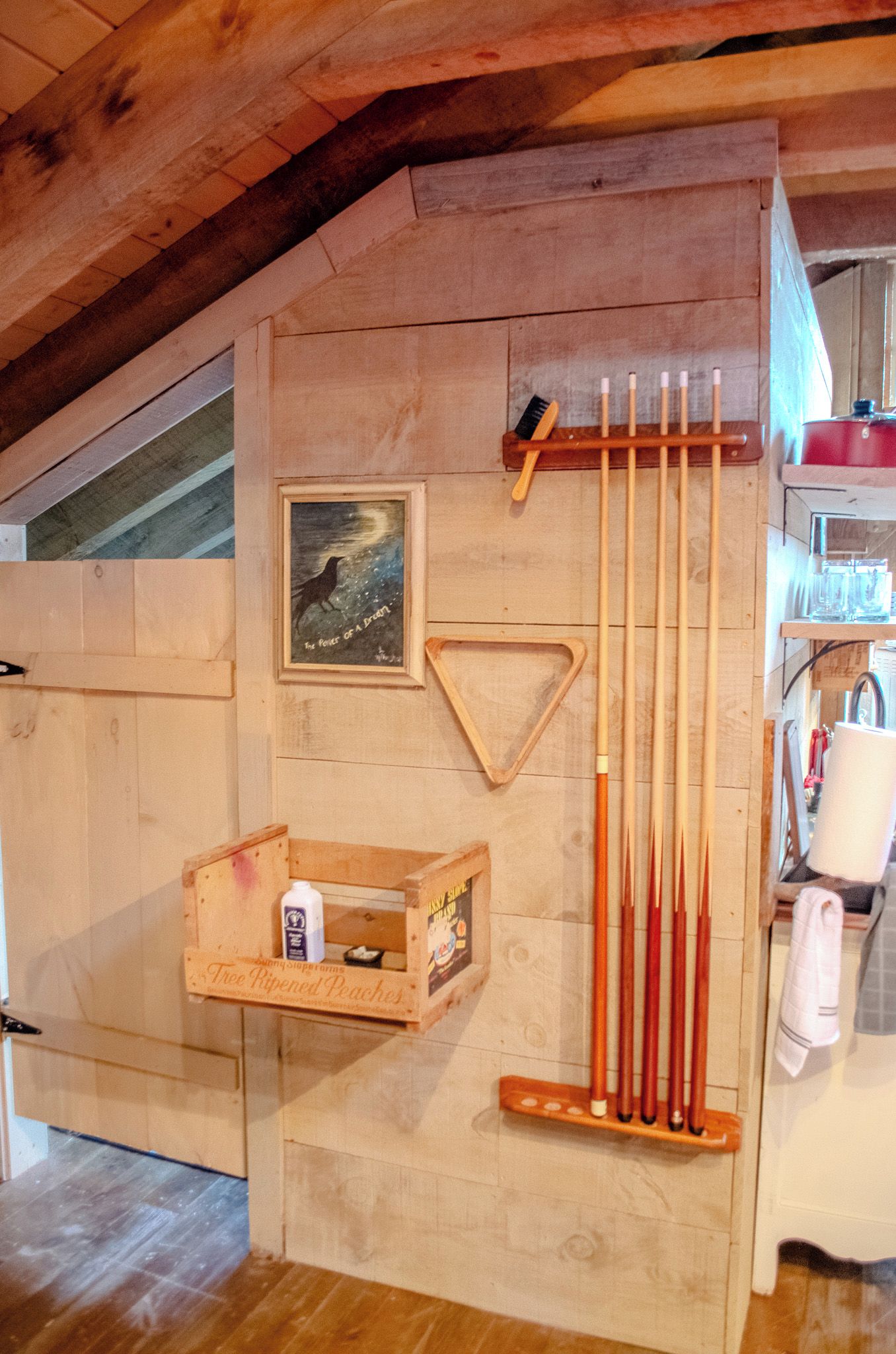 A wooden room with a sloped ceiling, a framed picture, a triangular wooden decoration, and a rack holding several wooden sticks.