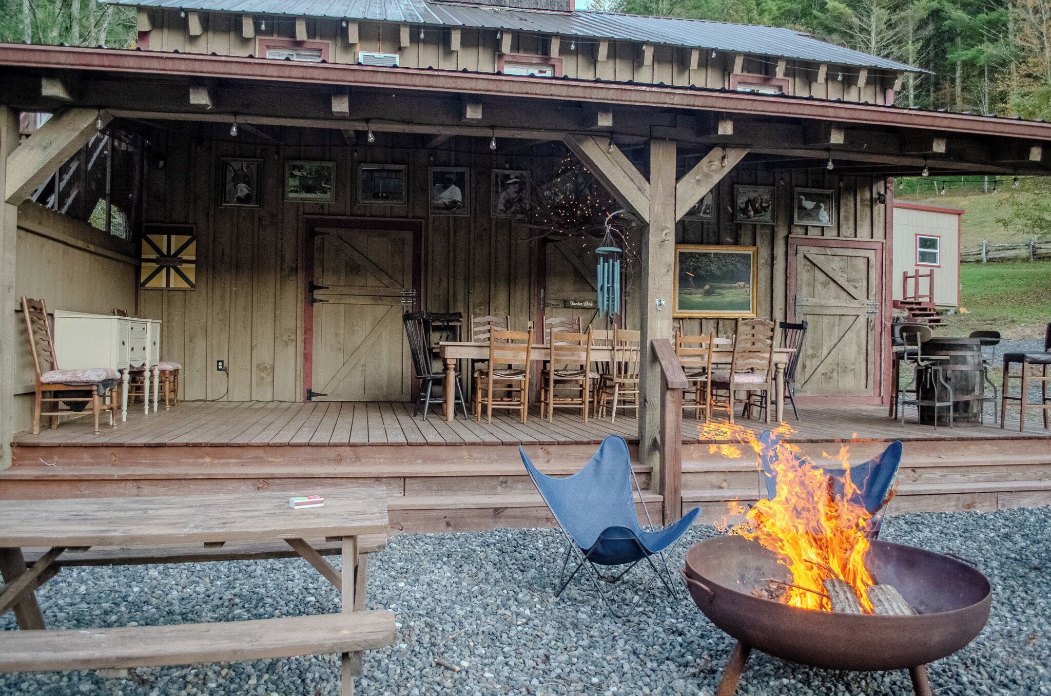 A rustic wooden building with a covered porch, outdoor seating, and a fire pit.