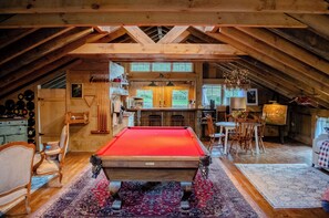 Um quarto de sótão acolhedor com mesa de bilhar, vigas de madeira, área de jantar e cozinha com amplas janelas.