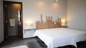 A hotel room with a bed, bedside tables, a mirror, and a wooden wall decoration. - Lost & Found Hostel & Suites (Albufeira)