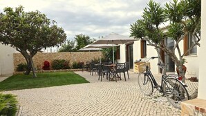An outdoor patio with tables and chairs, a stone wall, and a bicycle. - Lost & Found Hostel & Suites (Albufeira)