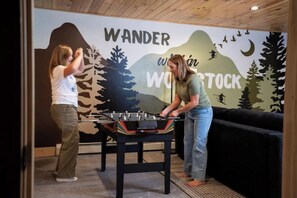 Two people playing foosball in a room with a wall mural depicting a mountainous landscape and the words "WANDER WITHIN WONDERS." - Nature Retreat, Sauna, Hot Tub, Gameroom, Fire Pit (Woodstock)