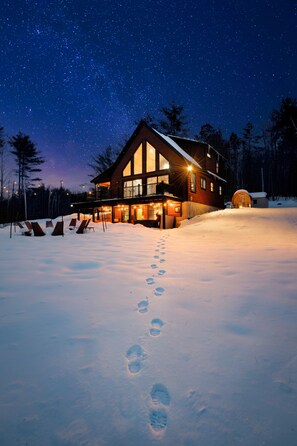 Ein großes Chalet mit einem Balkon mit Blick auf eine verschneite Landschaft bei Nacht.