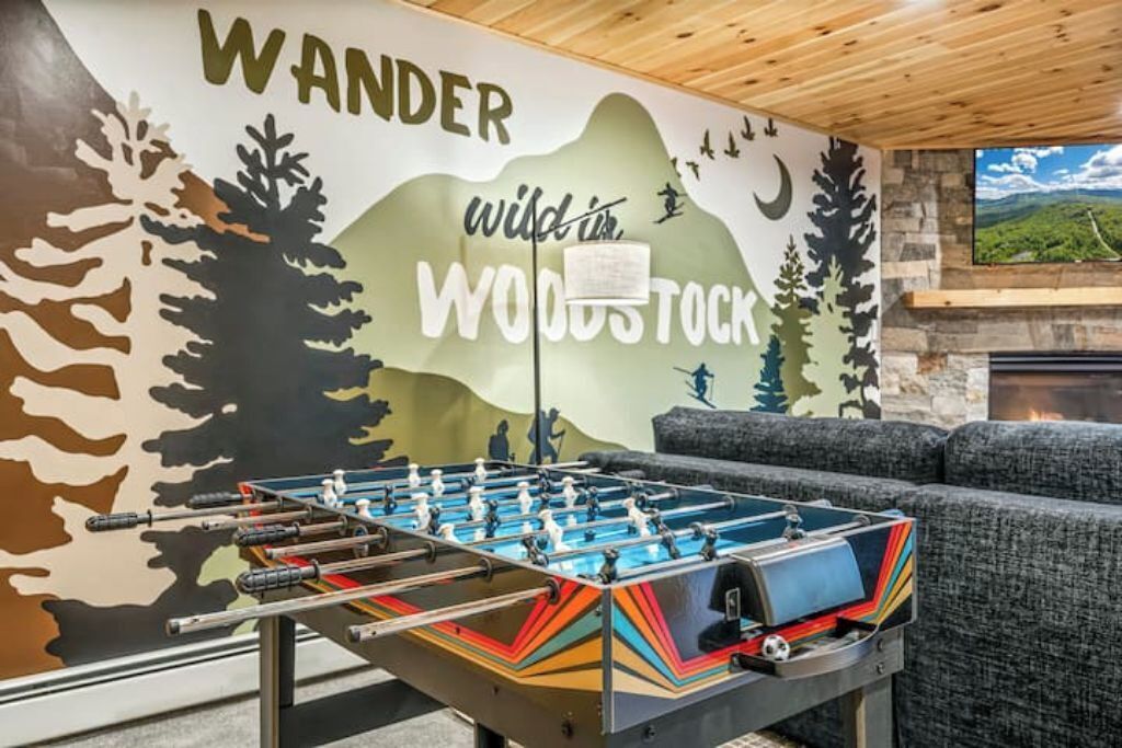 Una mesa de fútbolín en una habitación con un mural que representa un bosque y el texto "Wander wild in the WOODS TOCK".