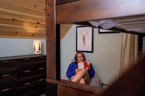 A person sitting on a bed in a room with wooden walls and a ceiling, reading a book. - Nature Retreat, Sauna, Hot Tub, Gameroom, Fire Pit (Woodstock)
