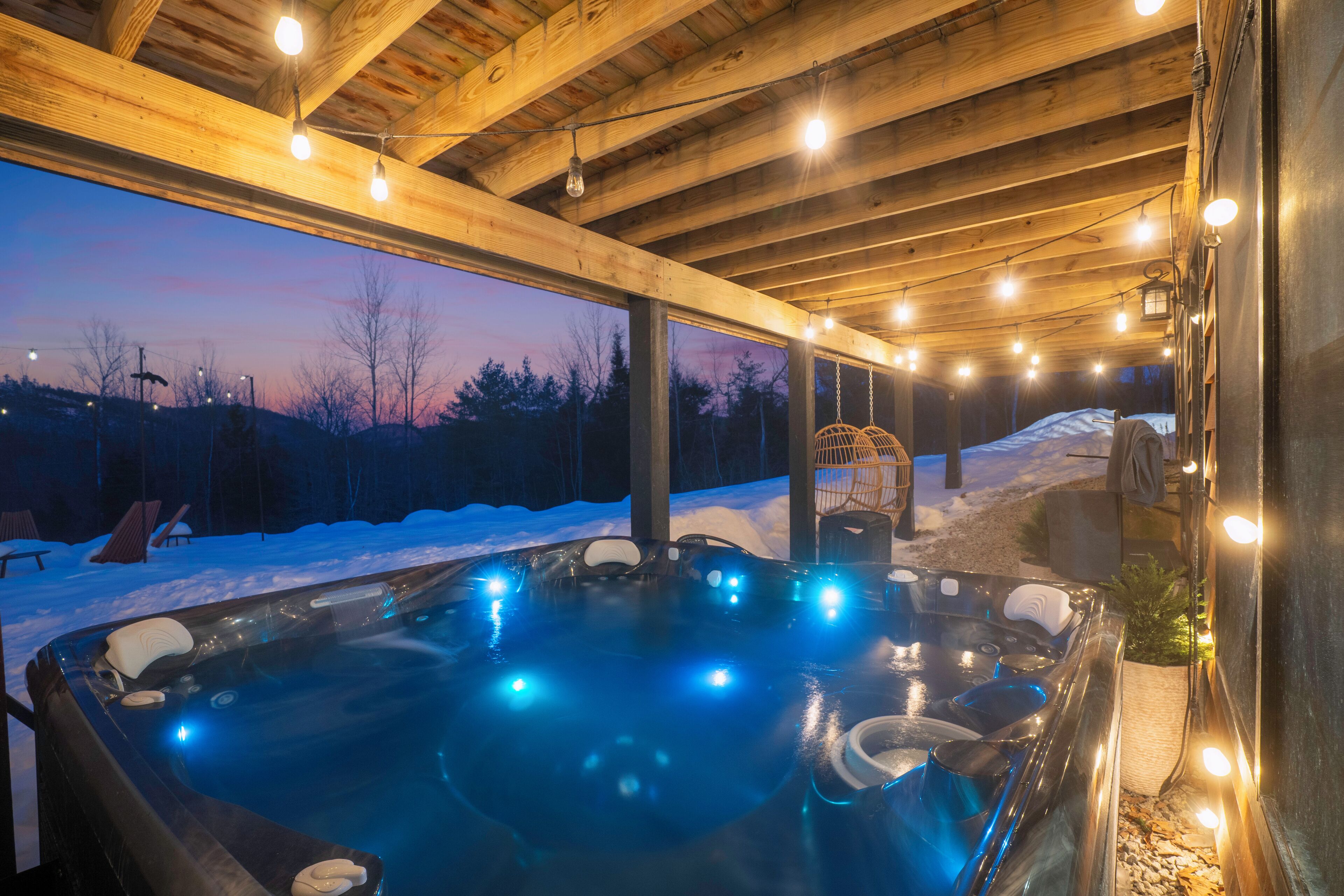 Een hottub met verlichting, houten balken en een besneeuwd buitengebied.