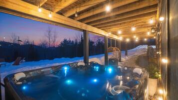 Een hottub met verlichting, houten balken en een besneeuwd buitengebied.