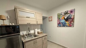 Una cocina moderna con microondas, pileta y muebles de madera. Se observa una obra de arte colorida en la pared y un objeto decorativo pequeño en la mesada.