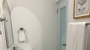 Un baño con lavamanos blanco, espejo, toallero, inodoro y zona de ducha.