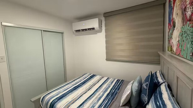 Un dormitorio con cama, armario, ventana con persianas y aire acondicionado.
