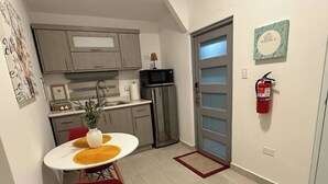 A compact kitchen with a dining area, a refrigerator, a microwave, and a fire extinguisher on the wall.
