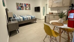 A modern apartment with a bed, a dining area with yellow chairs, a kitchen with wooden cabinets, and a fire extinguisher. - A&E L.A. Rental Apartments #2 (Carolina)