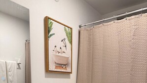 A bathroom with a white sink, a toilet, a shower curtain, and a framed picture on the wall. - A&E L.A. Rental Apartments #2 (Carolina)
