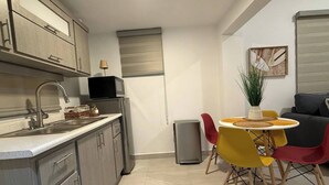 A compact kitchen with a sink, microwave, and refrigerator. There is a dining area with a table and chairs. - A&E L.A. Rental Apartments #6 (Carolina)