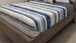 A neatly made bed with a striped bedspread, a wooden headboard, and a nightstand with a lamp. - A&E L.A. Rental Apartments #6 (Carolina)