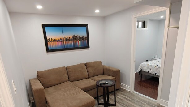 A modern living room with a brown sectional sofa, a small round table, and a cityscape painting on the wall.